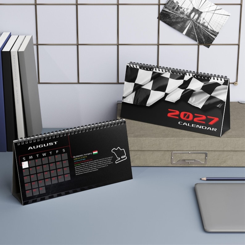 May include: A 2027 desk calendar featuring a black and white checkered flag design on the cover. The open page displays the month of August with a grid, a small map of the Budapest, Hungary race track, and descriptive text in English.