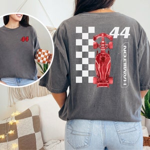 K&ouml;nnte beinhalten: Ein graues T-Shirt mit einem roten Rennwagen-Motiv und der Nummer 44 sowie dem Wort HAMILTON auf der R&uuml;ckseite.