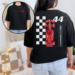 K&ouml;nnte beinhalten: Schwarzes T-Shirt mit einem roten Rennwagen-Motiv und der Nummer 44 auf der R&uuml;ckseite. Das Auto befindet sich auf einem karierten Flaggenhintergrund mit dem Wort "HAMILTON", das vertikal auf der rechten Seite gedruckt ist.