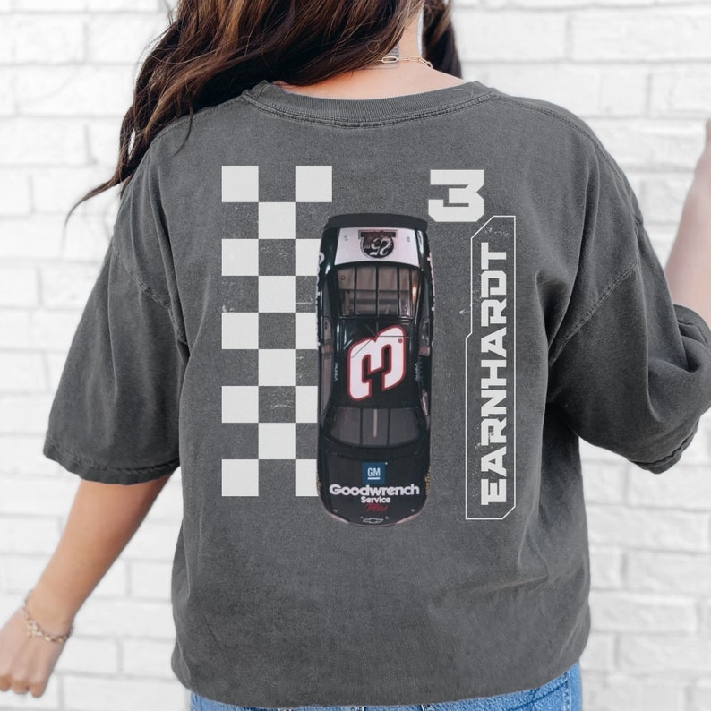 May include: A charcoal grey t-shirt with a vintage-style image of a black race car with the number 3 on it. The car is surrounded by a checkered flag pattern. The text "EARNHARDT" and the number "3" are printed vertically on the right side of the shirt.