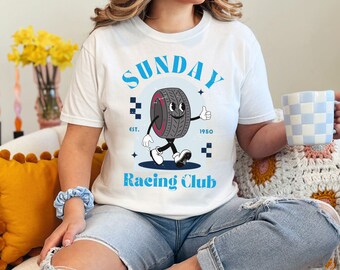 May include: White t-shirt with a blue and black graphic of a cartoon tire with a face and arms. The graphic says "Sunday Racing Club" with "Est. 1950" below it.