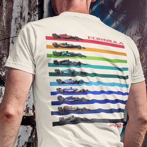 以下が含まれることがあります： 2021年のシーズンからのフォーミュラ1レーシングカーのカラフルなデザインが施された白いTシャツ。車はそれぞれのチームカラーとスポンサーで縦に並んでいます。「FORMULA」という文字は車の真上に赤で印刷され、「2021」という文字は車の真下に赤で印刷されています。