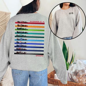 May include: Grey sweatshirt with a colourful stripe design featuring Formula 1 racing cars and the text "FORMULA 2025" on the back. The front of the sweatshirt has a small chequered flag design.