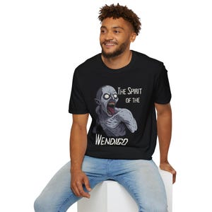 May include: Black t-shirt featuring a gray illustration of a creature with sharp teeth and an open mouth. The text "The Spirit of the Wendigo" is printed in white above and below the creature's image. The shirt is made of a soft material.