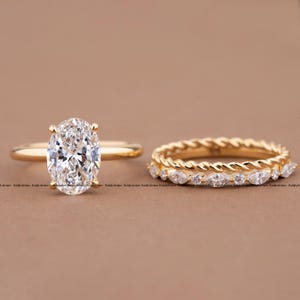 May include: A gold engagement ring featuring a large oval-cut centre stone and a matching gold wedding band. The band consists of a twisted rope design stacked with a row of marquise-cut stones, creating a two-piece ring set.