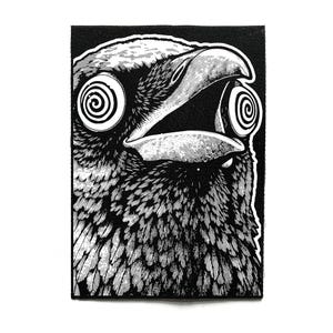 以下が含まれることがあります： くちばしを開けた鳥の様式化されたイラストが描かれた、長方形の白黒の刺繍ワッペン。鳥の目には渦巻き模様が施されており、コントラストの強い黒いインクでデザインが表現されています。