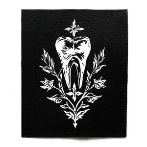May include: Black square patch with a white illustration of a tooth, surrounded by floral and cross-like elements. The tooth is the central focus, with detailed lines and a stylized design. The design includes leaves and a starburst at the top.