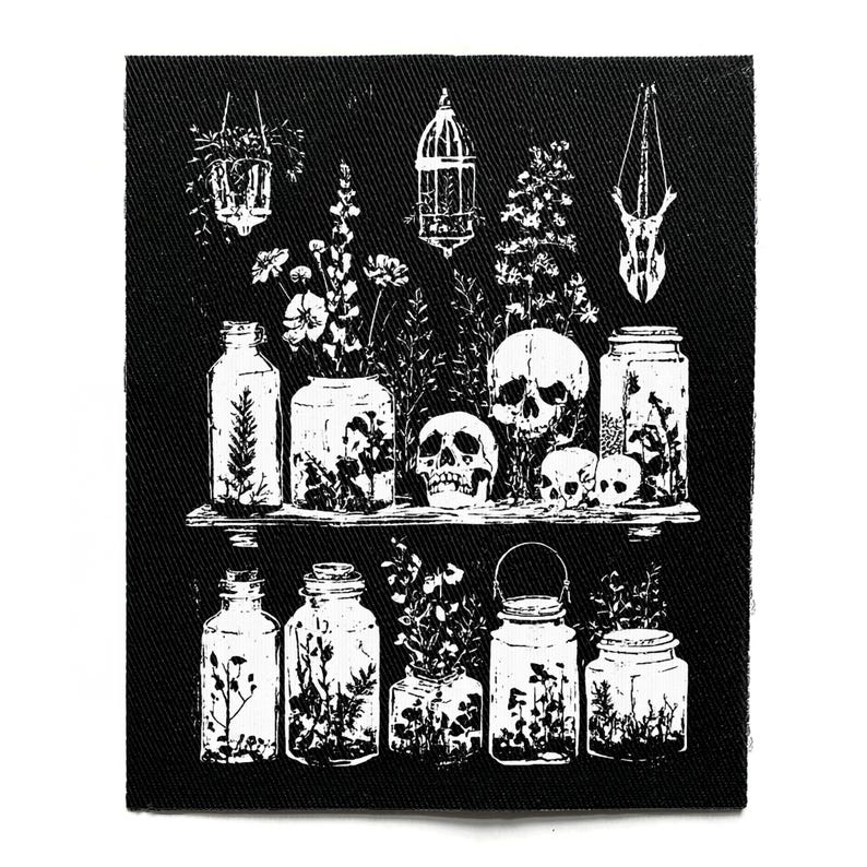 Puede incluir: Parche en blanco y negro que representa una estanter&iacute;a con tarros, flores y calaveras. El dise&ntilde;o incluye plantas colgantes, una jaula para p&aacute;jaros y un objeto con forma de calavera. El parche es rectangular y de tela.