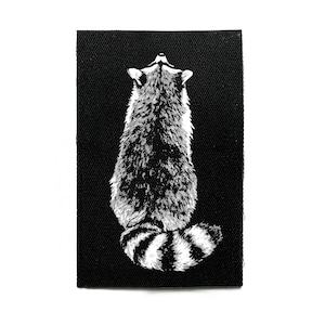 Peut inclure: Un écusson rectangulaire noir avec une illustration détaillée en noir et blanc d'un raton laveur vu de dos. La fourrure du raton laveur est texturée, et sa queue rayée est visible. Idéal pour les vêtements ou accessoires.