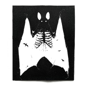 Può includere: Toppa in bianco e nero con un design di pipistrello scheletrico. Il corpo del pipistrello è una gabbia toracica, con grandi ali bianche e piccole sagome di pipistrelli. La toppa è rettangolare e ha un bordo in tessuto nero.
