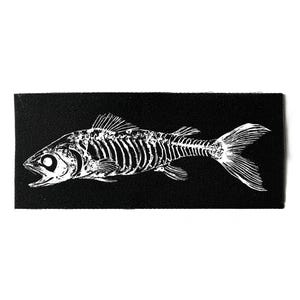 Peut inclure: Un patch rectangulaire noir avec une illustration blanche d'un squelette de poisson. Le poisson est représenté de profil, avec des côtes détaillées, des nageoires et un œil proéminent. Le design contraste fortement avec le fond noir.