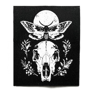 May include: Black and white patch featuring a moth above a skull, with a full moon in the background. The moth has detailed wing patterns. Floral elements surround the skull. The design is printed on a square black fabric.