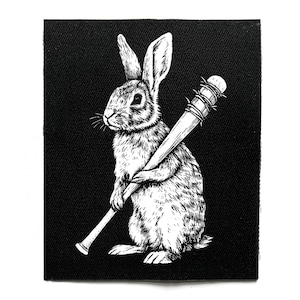 Op de afbeelding: Zwart-wit patch met een gedetailleerde illustratie van een konijn dat een honkbalknuppel met prikkeldraad vasthoudt. Het konijn is afgebeeld tegen een effen zwarte achtergrond. De patch is vierkant.