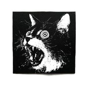 May include: Square black and white patch depicting a screaming cat with exaggerated features. The cat has large, spiral eyes and an open mouth revealing teeth. The design is bold, with white fur against a black backdrop.