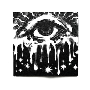Könnte beinhalten: Quadratischer schwarz-weißer Aufnäher mit einer Augenillustration, stilisierten Tränen und radialen Linien. Das Design beinhaltet Sterne am unteren Rand, was eine mystische Ästhetik erzeugt. Der Aufnäher ist aus Stoff.