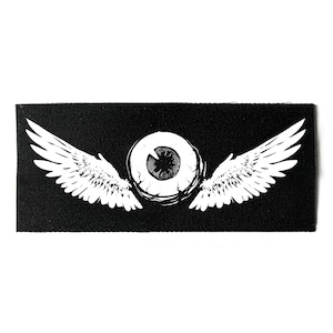 Könnte beinhalten: Schwarzer rechteckiger Aufnäher mit einem weißen Augendesign, detaillierter Iris und weißen Flügeln. Die Flügel sind symmetrisch und erstrecken sich nach außen. Der Aufnäher besteht aus einem strukturierten Stoff.