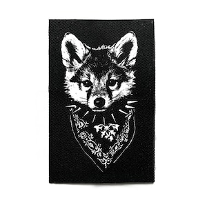 May include: Black and white patch featuring a stylized fox head with a bandana. The fox has a detailed face and is wearing a bandana with a floral design and spikes. The patch is rectangular and has a textured appearance.
