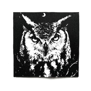 Könnte beinhalten: Quadratischer schwarz-weißer Aufnäher mit einer detaillierten Eulenillustration. Über dem Kopf der Eule befindet sich ein Halbmond. Der Aufnäher hat eine strukturierte Oberfläche.