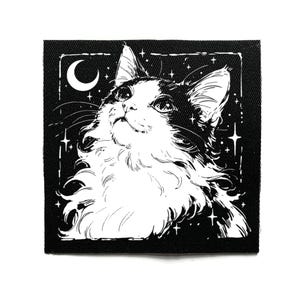 Puede incluir: Parche cuadrado en blanco y negro que representa un gato mirando una luna creciente y estrellas. El gato tiene pelaje esponjoso y está sobre un fondo de cielo estrellado. El parche es de forma cuadrada.