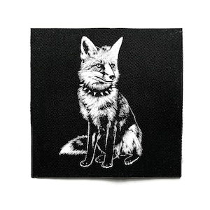 May include: A black square patch with a white illustration of a fox wearing a studded collar. The fox is depicted in a seated position, with its head turned to the right. The patch has a textured finish.