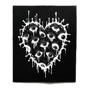 Puede incluir: Parche cuadrado negro con un diseño blanco en forma de corazón lleno de múltiples ojos. Los ojos tienen iris detallados y están rodeados por un borde goteante. El parche está hecho de tela texturizada.