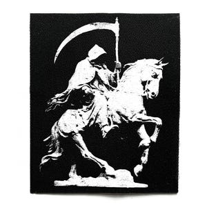 Puede incluir: Parche en blanco y negro que representa la Muerte a caballo. La Muerte, con capa y capucha, sostiene una guadaña. El caballo se alza sobre sus patas traseras, creando una imagen dinámica. El parche tiene una superficie texturizada.