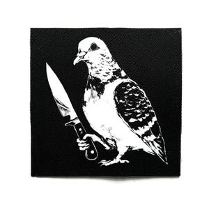 Può includere: Toppa in bianco e nero raffigurante un piccione che tiene un coltello. Il piccione è illustrato in dettaglio, con il coltello come elemento centrale. La toppa è quadrata e posta su uno sfondo nero.