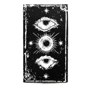 May include: Black rectangular patch with a white design of three eyes, one with radiating lines, and stars. It has a distressed white border. Suitable for clothing or accessories.