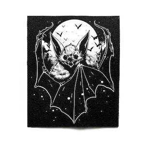 May include: Black and white patch featuring a detailed illustration of a bat with large ears and spread wings. The bat is set against a backdrop of a full moon, with silhouettes of flying bats and trees. The patch has a textured appearance.