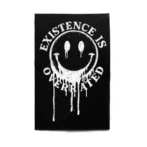 May include: Black rectangular patch with a white smiley face design. The smiley face has a dripping effect, and the text "EXISTENCE IS OVERRATED" is printed around the face in a circular pattern.