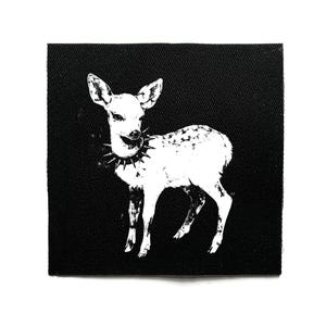 May include: A black square patch with a white illustration of a deer wearing a spiked collar. The deer is depicted in a standing pose, with its head turned. The patch has a textured surface.
