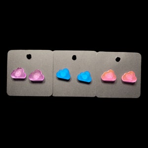 May include: Three sets of cloud-shaped earrings on display cards. The first set is purple, the second is blue, and the third is pink.