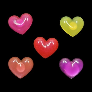 May include: Six heart-shaped candies in different colors: pink, red, yellow, orange, and purple. The candies are on a black background.