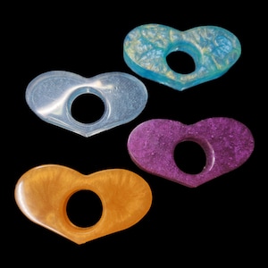 May include: Four heart-shaped resin rings in different colors: light blue, clear, purple, and orange. Each ring has a hole in the center.