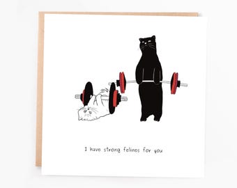 May include: A greeting card with a black and white illustration of two cats. One cat is lifting weights, while the other cat is lying on the ground. The text on the card reads "I have strong felines for you."