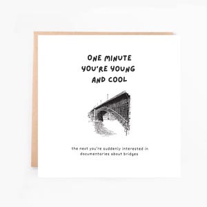 May include: A square greeting card with a brown border. The card features the text "ONE MINUTE YOU'RE YOUNG AND COOL" above a black and white illustration of a bridge. Below the bridge is the text "the next you're suddenly interested in documentaries about bridges."