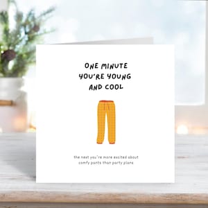 Könnte beinhalten: Eine weiße Grußkarte mit dem Text "ONE MINUTE YOU'RE YOUNG AND COOL" und "the next you're more excited about comfy pants than party plans." Die Karte zeigt eine Illustration einer gelben Hose.