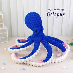 May include: A large, handmade blue crochet octopus with white and pink accents on its tentacles. The text "PDF PATTERN Octopus" is visible. The octopus is a soft toy, likely for children or as a decorative item.