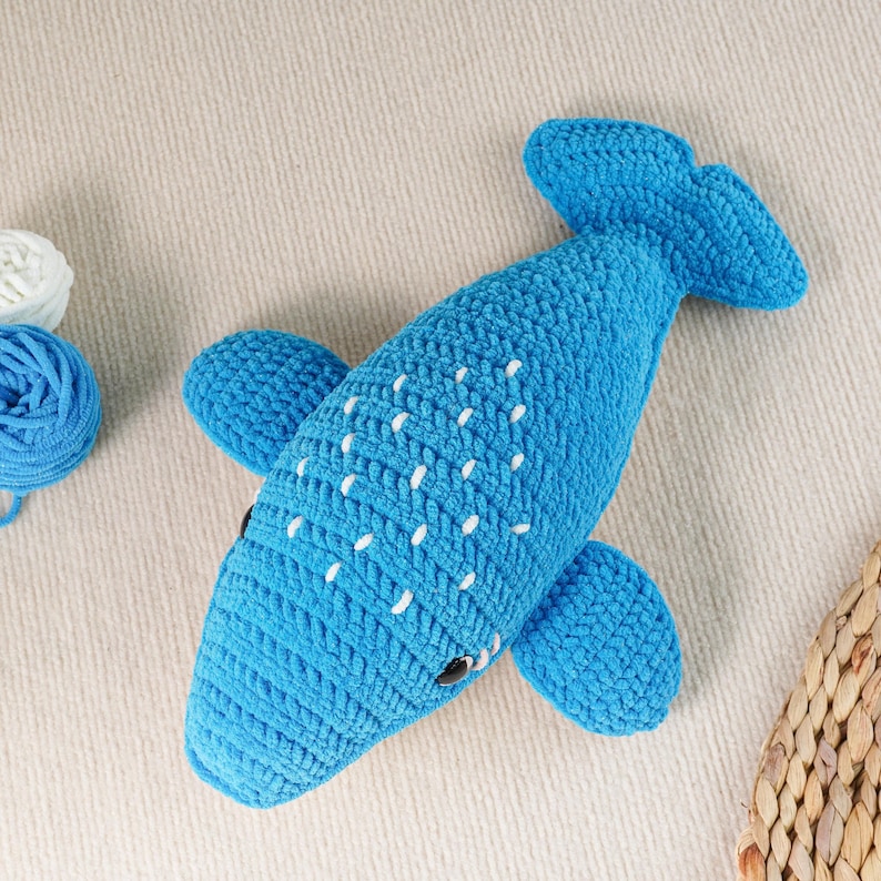 May include: A handmade blue crochet whale toy with white dotted accents. The whale has fins, a tail, and small black eyes. The toy is made of soft yarn and is a cute, cuddly item.