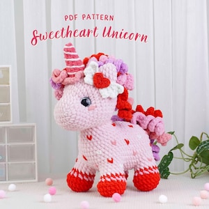 Puede incluir: Un unicornio rosa tejido a ganchillo con detalles rojos y blancos. El unicornio tiene un cuerno a rayas, un adorno en forma de flor y una melena rizada. El texto "PDF PATTERN Sweetheart Unicorn" se muestra arriba.