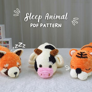 Puede incluir: Tres juguetes de animales durmientes de ganchillo: un panda rojo, una vaca y un tigre. El panda rojo es naranja y marrón, la vaca es blanca con manchas negras y el tigre es naranja con rayas negras. Se muestra el texto "Sleep Animal PDF Pattern".
