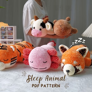 May include: Five crocheted stuffed animals in various colours and designs, including a tiger, cow, axolotl, red panda, and a brown bear. The animals are all lying down with their eyes closed, as if they are sleeping. The text "Sleep Animal PDF Pattern" is written below the animals.