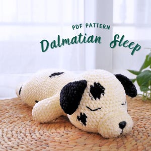 Puede incluir: Patrón PDF para tejer un juguete de peluche de perro dálmata durmiendo. El juguete es blanco con manchas negras y tiene los ojos cerrados. El juguete está acostado en una estera tejida.