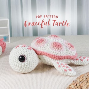 Puede incluir: Una tortuga de ganchillo en blanco y rosa, con una cabeza grande y redonda y un caparazón. El texto "PDF PATTERN Graceful Turtle" se muestra encima de la tortuga. Hay ovillos de lana en el fondo.