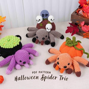 Op de afbeelding: Een verzameling handgemaakte gehaakte Halloween-decoraties, waaronder spinnen, een ketel en een pompoen. De spinnen zijn paars, grijs en oranje. De tekst "PDF Pattern Halloween Spider Trio" is inbegrepen.