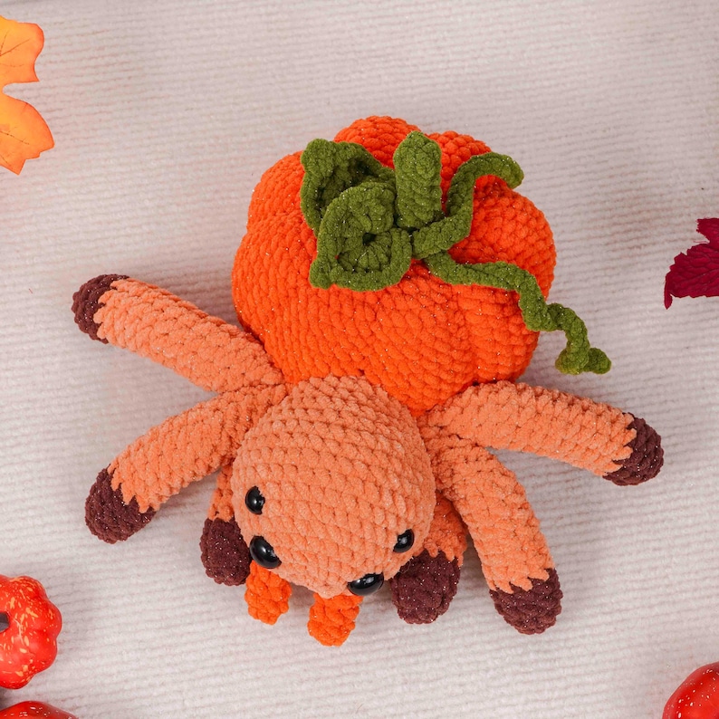 May include: A handmade orange and brown crochet spider with a pumpkin head. The spider has eight legs, each with dark brown tips. The pumpkin head is orange with green leaves and a stem. A fun Halloween decoration.