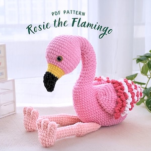 May include: A handmade pink crochet flamingo with a black beak, yellow accents, and a white and red ruffled design. The text "PDF PATTERN" and "Rosie the Flamingo" are visible. The flamingo is sitting on a white surface.