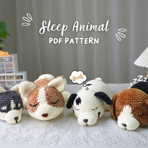 Könnte beinhalten: Vier gehäkelte Stofftiere in Form von schlafenden Hunden. Die Hunde sind braun, schwarz, weiß und beige. Die Hunde liegen auf einer weißen Oberfläche. Der Text "Sleep Animal PDF PATTERN" befindet sich über den Hunden.