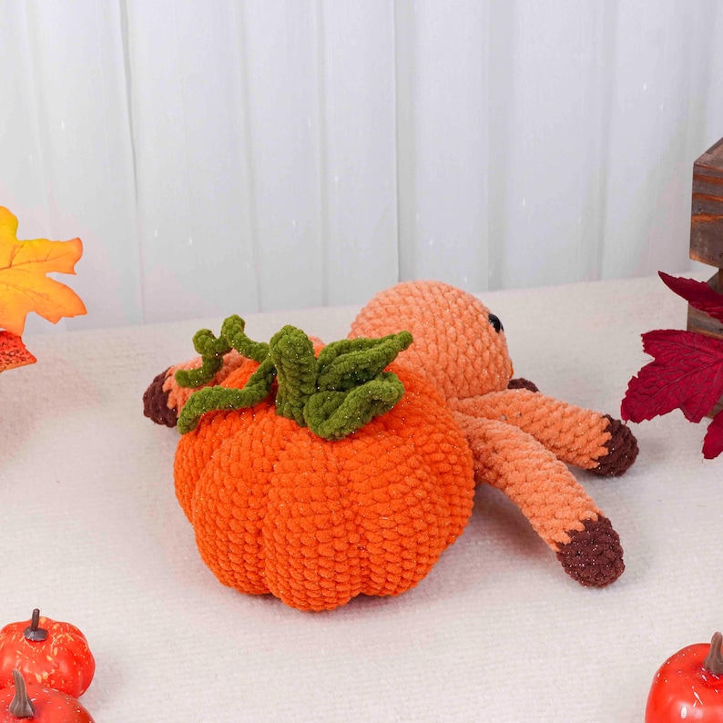 May include: An orange crochet pumpkin with green leaves and a brown stem next to an orange octopus plushie. The octopus has brown tips on its tentacles. The items are on a white surface with fall leaves.