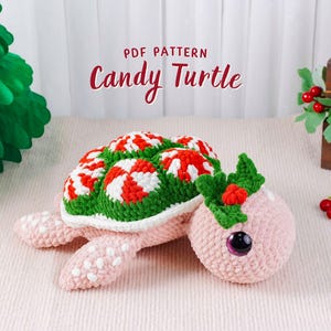 May include: A handmade crochet turtle with a candy-themed design. The turtle's shell features red and white peppermint candy patterns on a green background. The head is pink with a green holly accent and a black eye. The text "Candy Turtle" is displayed.